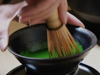 Whisking matcha in a matte black tenmoku chawan tea bowl with bamboo chasen whisk, traditional tea ceremony style
