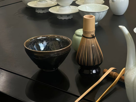 Home tea corner on dark wood - black glazed Jian Zhan bowl, bamboo chasen whisk and bamboo tools with white porcelain teaware
