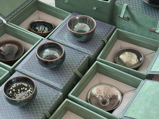 Jian Zhan tea bowls with varied oil spot and hare's fur glazes arranged in green presentation boxes for inspection