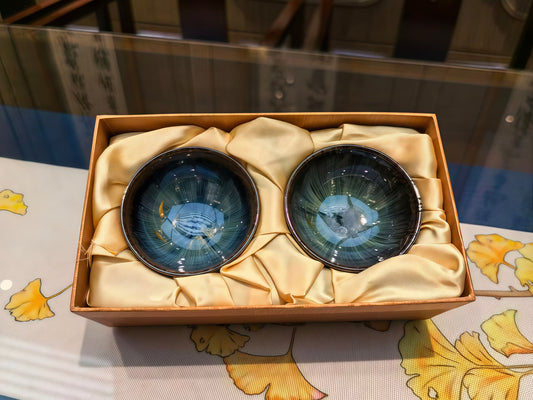 Two blue glazed Jian Zhan cups in a wooden gift box lined with gold silk, ready for holiday gifting